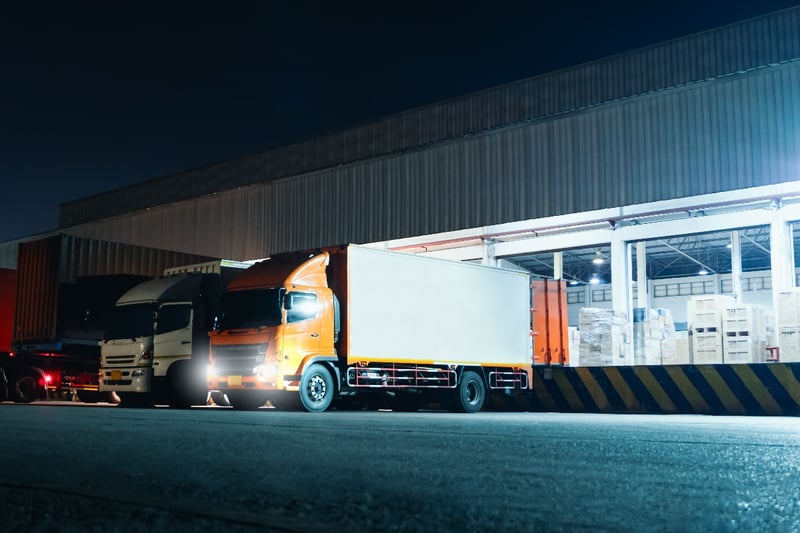 A group of semi-trucks being unloaded at a distribution center. 