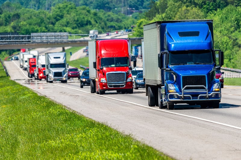 Several semi-trucks sit in traffic on a crowded highway. 