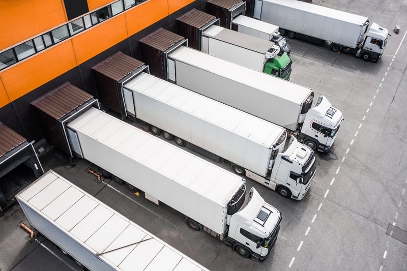 Several semi-trucks being loaded at a busy distribution center.