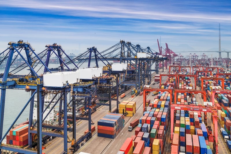 A semi-truck drives through a busy industrial port filled with containers. 