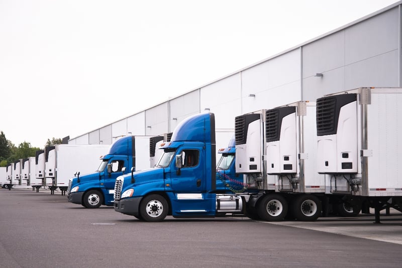 A group of semi-trucks being loaded at a distribution center.
