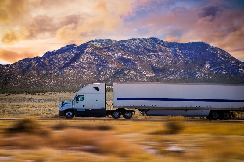 A semi-truck carrying cargo drives down a scenic mountain highway in Colorado.